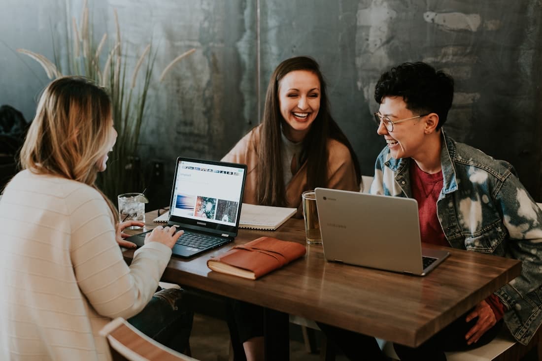 Three friends laughing together at a table with laptops